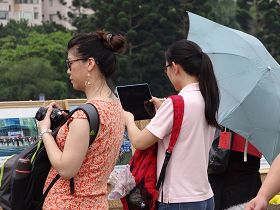 二位遊客，一位用ipad，一位用相機，將展示的法輪功真相圖片一張張拍下來。