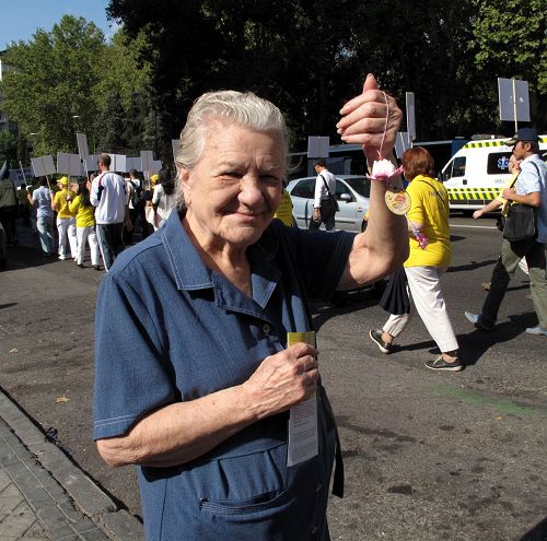 圖4：法輪功學員在馬德裏舉行大遊行，一位西人老太太站在路旁從頭到尾觀看遊行隊伍，照相時，她高興地舉起前面經過的法輪功學員送給她的手工蓮花