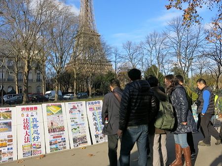 法國的法輪功學員在巴黎艾菲爾鐵塔旁設立了真相點，成群結隊的中國遊客經過這裏時，有許多人觀看和閱讀展板了解真相。