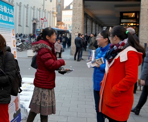 '圖6：慕尼黑的法輪功信息展位上，一位法輪功學員（左）正在向兩位華人講述法輪功真相。'