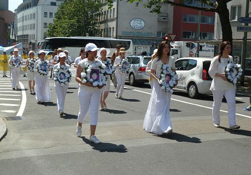 最後面是神情肅穆，身著白衣的女法輪功學員，她們每人手捧一個圓盤，上面是一位在中國被迫害致死的法輪功學員的照片。
