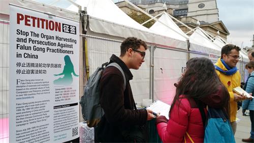 圖3：二零一八年十月二十七日，倫敦學生西奧（Theo，左）在特拉法加（Trafalgar Square）廣場與法輪功學員一起向路人發真相傳單、徵簽