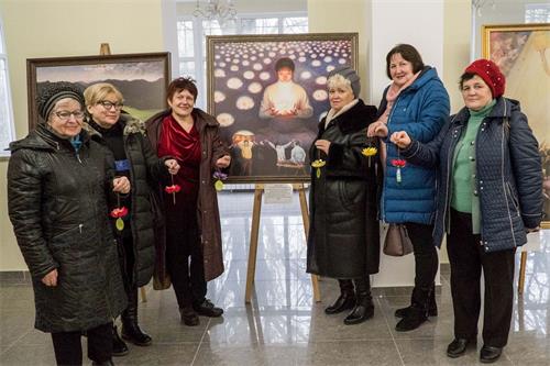 '圖1：觀看畫展的俄羅斯民眾手持紙蓮花和法輪功學員創作的畫合影'