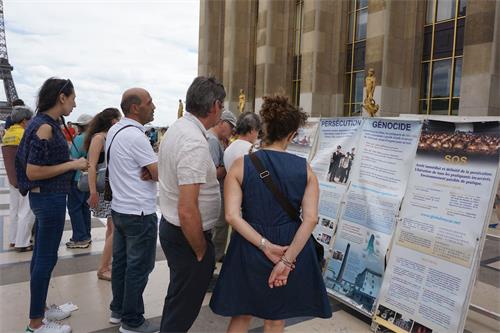 '圖1～2：巴黎人權廣場上，過往遊客認真閱讀法輪功真相展板'