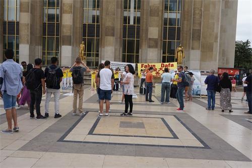'圖3：巴黎人權廣場上，過往遊客認真閱讀法輪功真相展板，觀看法輪功學員煉功。'