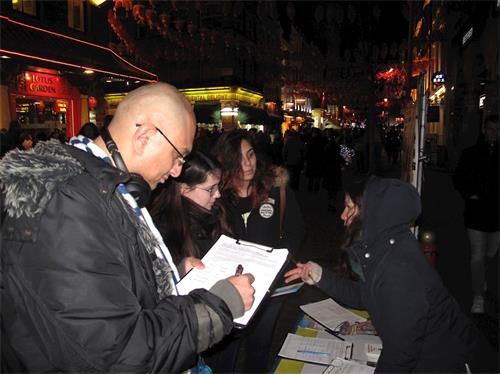 '圖4：二零一九年二月十日，在倫敦唐人街，一位在倫敦工作的孟加拉裔男士（左）和兩位從巴西來倫敦旅遊的女青年駐足傾聽真相，接著簽名支持法輪功學員反迫害'