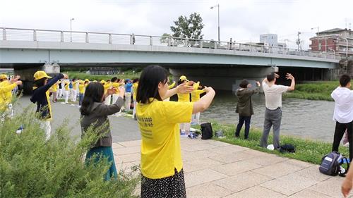'圖1～2：當天早晨九點到十一點，法輪功學員在京都市政府附近的御池大橋（Oike-ohashi Bridge）下鴨川河畔的集體煉功，吸引了許多有緣人駐足了解法輪功。'