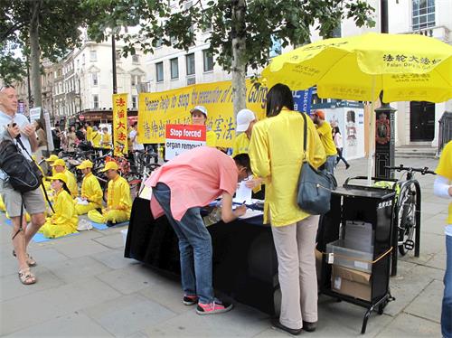 '圖5：二零一九年七月二十日，在倫敦聖馬丁廣場，一位在英國留學的香港青年聽法輪功學員講真相，在法輪功反迫害徵簽表上簽名。'