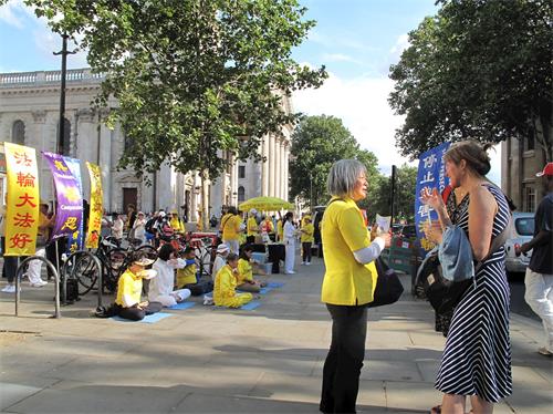 '圖7：二零一九年七月二十日，在倫敦聖馬丁廣場，這女士（右）被法輪功功法演示所吸引，詢問學員真相，並在反迫害徵簽表上簽了名。'