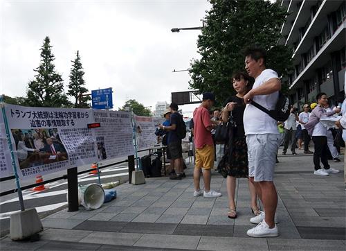 '圖6～7：日本法輪功學員在東京九段下車站擺展板，講真相，民眾駐足閱讀展板。'