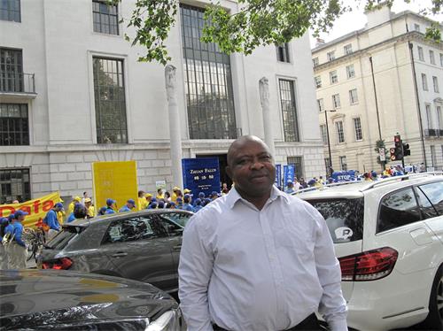 '圖10：八月三十日，在倫敦中使館前，在倫敦銀行工作的西爾維塞爾（Sylveseer）駐足聆聽並拍攝法輪功學員的新聞發布會'