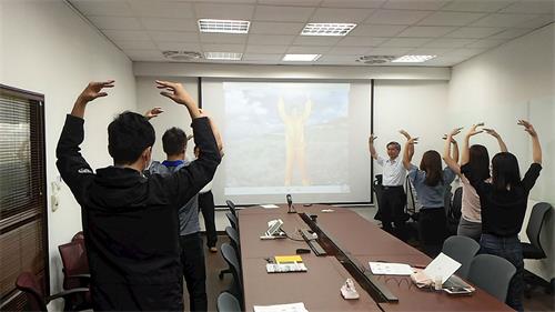 '圖1：在公司會議室裏舉辦的法輪功九天學法班，新學員們跟著教功錄像帶煉功。'