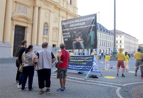 '圖1：二零二零年八月八日，法輪功學員在德國慕尼黑的奧迪安廣場（Odeonsplatz）舉辦信息日活動。圖為揭露中共活摘法輪功學員器官的大型圖畫。'