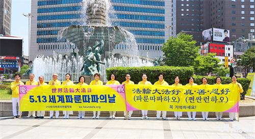 圖1：5月13日，部份首爾西部和中部的法輪功學員們在首爾市中心新世界百貨店附近的大型噴泉前舉行了集體煉功、派發傳單等洪法活動。圖為他們在活動前，首先恭祝慈悲偉大的師尊華誕。