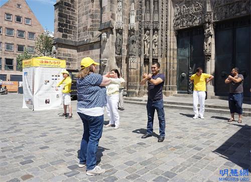 '圖2：二零二一年六月三日，法輪功學員在德國紐倫堡市的洛倫茲教堂前舉行信息日，兩位烏茲別克斯坦遊客當場學習法輪功功法。'
