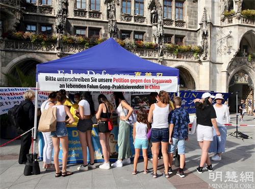 '圖1：二零二一年八月十日，德國法輪功學員在慕尼黑瑪琳廣場（Marienplatz）舉辦活動。圖為民眾排隊簽名聲援法輪功學員反迫害。'