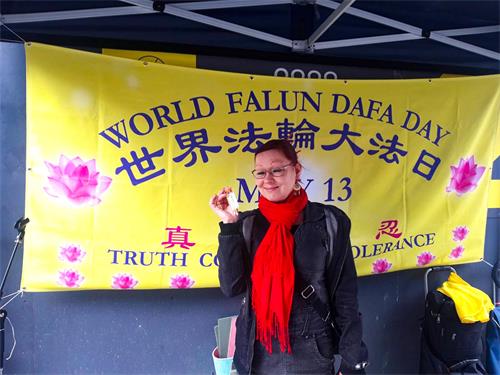 圖8：殘疾人指導教師T. Pyy女士手拿小蓮花，在「世界法輪大法日」橫幅前拍照留影