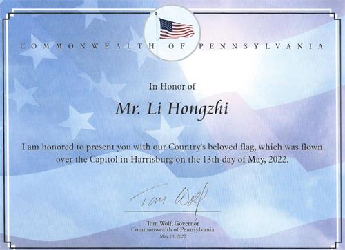 '圖2：賓州州長湯姆﹒沃爾夫（Tom Wolf）頒發證書，將這面「五﹒一三」飄揚在賓州國會大廈的美國國旗贈送給李洪志先生。'