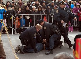 右圖：紐約法拉盛新年遊行活動中，一華裔男子從觀眾群中衝到法輪功隊伍的前面，拉扯橫幅並折斷橫桿。三個警察立即衝上去將其制服並逮捕。