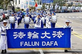 二零一零年十月在韓國仁川的一個市民節日遊行中，金先生手持指揮棒引領由法輪功學員組成的軍樂隊。