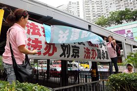 穿著粉紅色制服的「香港青年關愛協會」中共幫兇，用帶來的橫幅掩蓋法輪功學員的橫幅，故意挑釁香港法輪功學員。