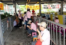 十多名身穿粉紅色統一制服，上印香港青年關愛協會的幫兇，十九日衝進法輪功學員真相點內，四處懸掛污衊橫幅，又大搖大擺吃東西，用盡各種方法挑釁。