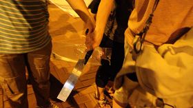 一名穿間條衫的女兇徒一度從另一名親共團夥徒眾手上接過鋸刀，準備趨前恐嚇記者。