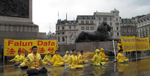 '二零一三年八月二十四日下午，英國法輪功學員冒雨在倫敦鴿子廣場中心演示法輪功功法，傳播真相。'