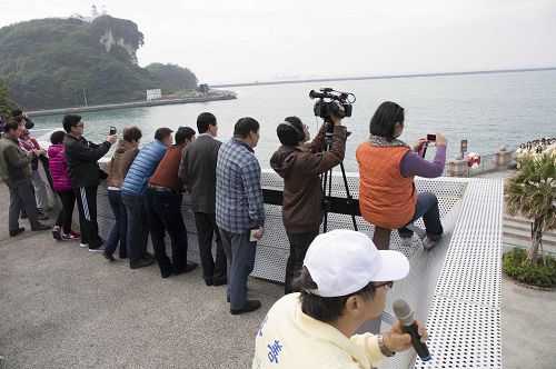 幾位大陸遊客快快登上雄鎮北門高處看台，拿起手機、相機拍下法輪功學員給師父拜年的合照。