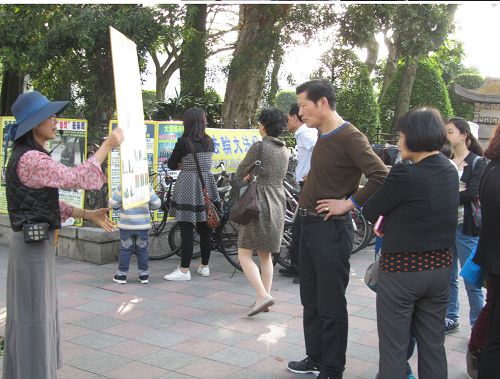 中國大陸遊客眼觀展板、耳聽法輪功學員講真相。