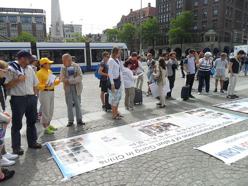 圖2-7：荷蘭學員在首都阿姆斯特丹達姆廣場向各國遊客傳播真相，他們有的認真閱讀真相展板，有的簽名支持制止迫害，起訴迫害元凶江澤民。