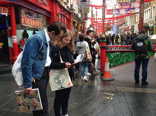 '圖6：二零一六年十月一日下午，在倫敦唐人街，法輪功學員的反迫害遊行隊伍經過後，一對年輕人在非常專注地閱讀真相傳單'