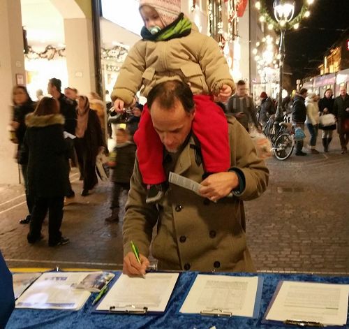 '圖7：一位德國男士頂著孩子認真的簽名支持法輪功'