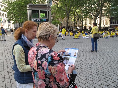 圖6：來自東歐的米麗娜女士（右）在紐約美國國家圖書館前一邊觀看法輪功學員集體煉功，一邊閱讀真相傳單。