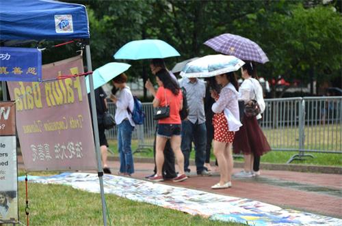 '圖7：集會期間下起了大雨，但中國大陸遊客仍冒雨觀看揭露中共迫害法輪功的真相展板。'