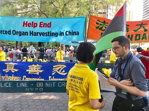 '圖1：福克斯新聞記者亞當﹒蕭（Adam Shaw，右）站在「請幫助結束發生在中國的大屠殺」（Help End Genocide in China）條幅前，採訪法輪功學員簡（Jane）。'
