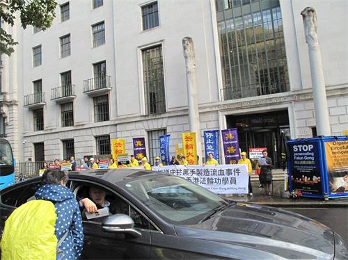 '圖3：英國法輪功學員在倫敦中使館前集會反迫害，路人和司機接過法輪功真相傳單。'