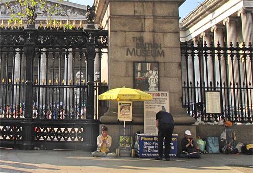 '圖15：二零一九年四月二十一日，大英博物館門前，兩位法輪功學員在打坐，一位西人默默走過來簽名。'