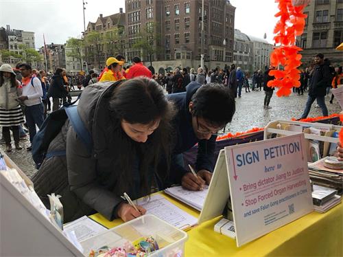 '圖3～4： 在首都阿姆斯特丹（Amsterdam）市中心──達姆（Dam）廣場上，遊客簽名支持法輪功反迫害。'