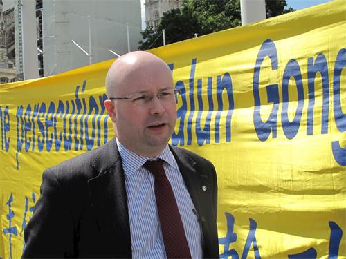 '圖10：二零一九年七月十六日，英國會議員帕特裏克﹒格雷迪（Patrick Grady MP）來到法輪功學員「反迫害二十週年」集會現場表支持，他站在「請伸出援手制止迫害法輪功（Please help to stop the persecution of Falun Gong）」橫幅前接受採訪'