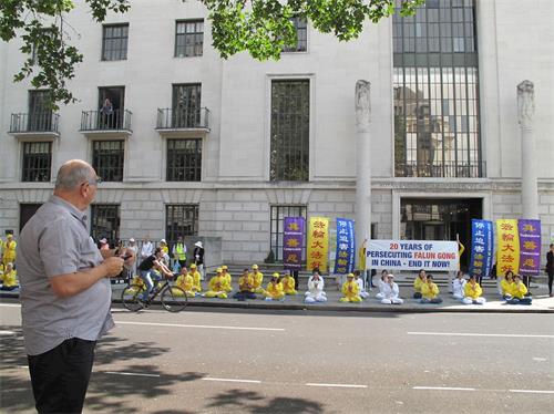 '圖1：二零一九年七月二十日，法輪功學員在倫敦中使館前煉功靜坐集會，路人駐足觀看。'