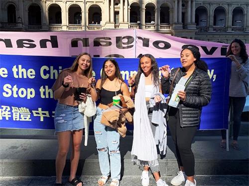 '圖13：四位澳洲女孩在了解法輪功真相後紛紛簽字呼籲停止迫害。她們手握法輪功學員送給她們的蓮花小吊墜，在制止迫害的真相橫幅前集體拍照。'