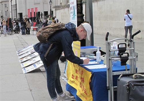 '圖9：二零二零年八月二十二日，在特拉法加廣場，在倫敦學醫的大學生帕特裏克（Patrick）簽名支持制止迫害。'