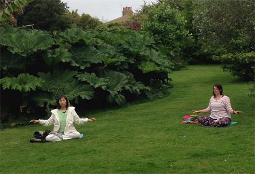 '圖2：二零二零年六月二十三日，英國法輪功學員羅斯（Rose，右）與英國日裔法輪功學員鶴田緣（Yukari）在茂拉博花園的草地上煉功打坐'