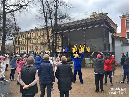 '圖1：二零二一年四月二十四日，俄羅斯聖彼得堡市法輪功學員在慶祝「世界太極拳和氣功日」活動中介紹和演示法輪功，台下的觀眾跟著學煉功法動作。'