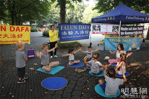 '圖5：二零二一年八月二十一日，法輪功學員在慕尼黑的霍亨索倫廣場（Hohenzollernplatz）舉辦活動。一群小朋友和一位德國婦女帶著孩子一起跟學員學煉打坐。'
