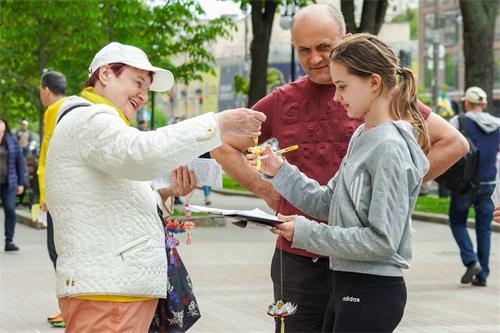 圖：烏克蘭法輪功學員瓦倫蒂娜（左）給基輔民眾發放真相資料和小蓮花