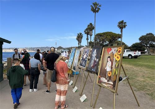 '圖4：二零二二年五月七日，聖地亞哥學員在拉荷雅（La Jolla）海邊洪法講真相，「真善忍美展」的畫作吸引遊人駐足觀看。'